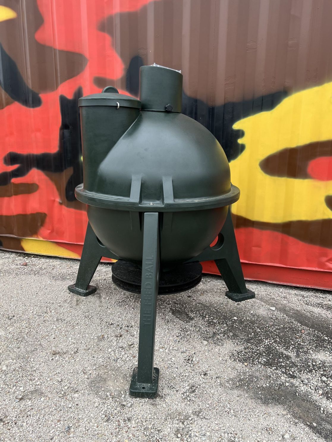 A green object is sitting on the ground in front of a camouflage wall.