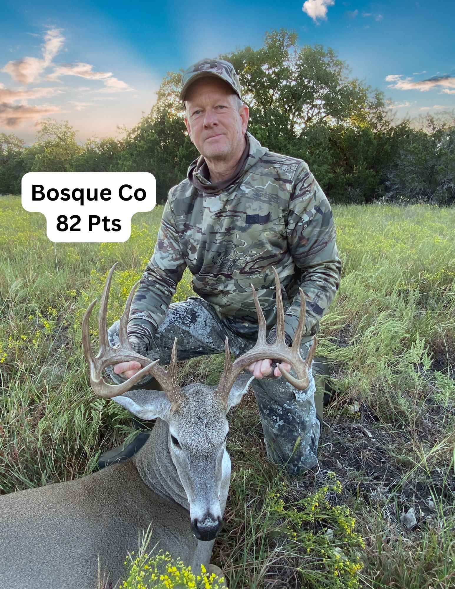A man is kneeling down next to a deer in a field.