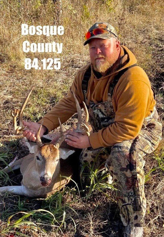 Man kneels with a deer he hunted in Bosque County, Texas. He wears orange and camo; the deer has antlers.