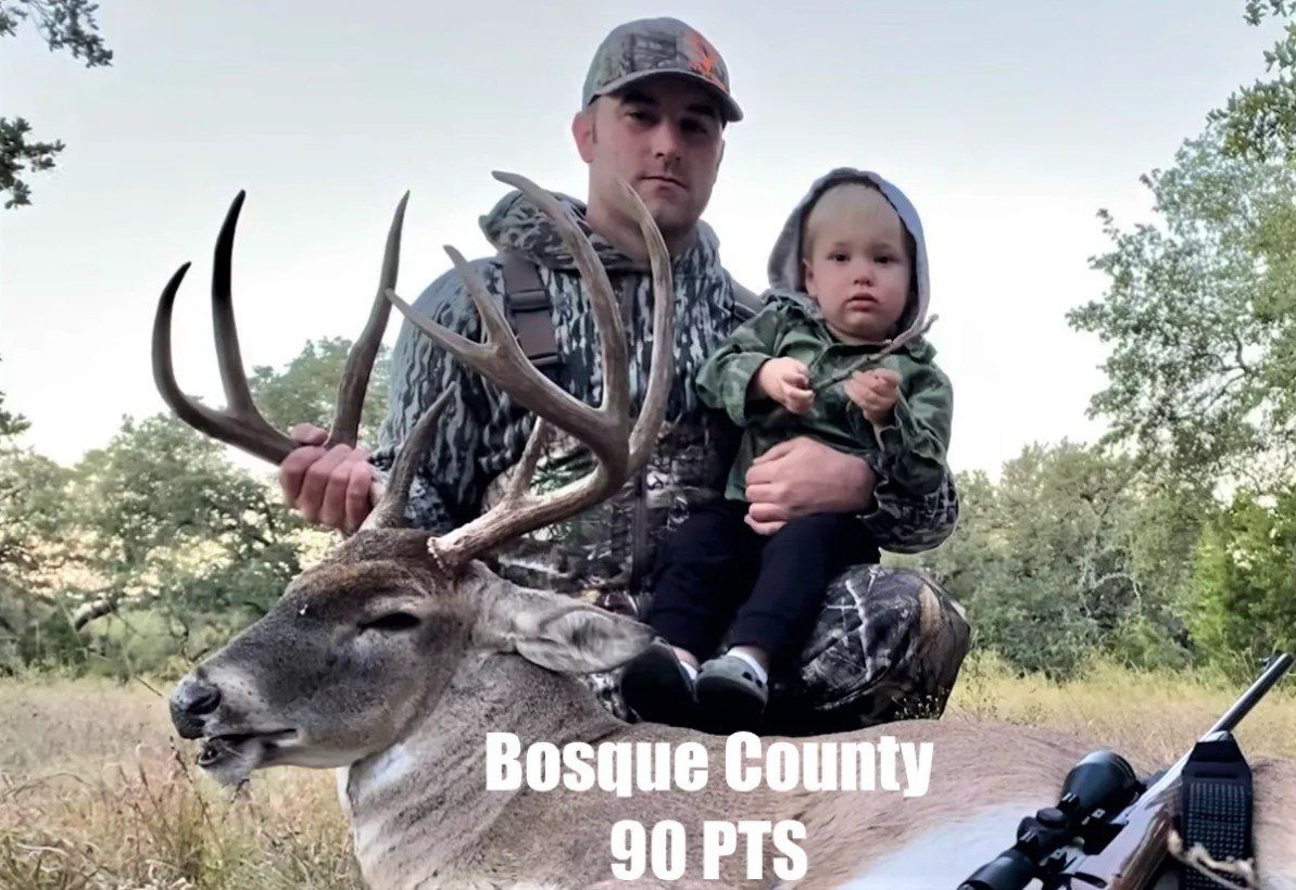 Man and child with a large buck in Bosque County, Texas. Hunter wears camo, child is held up. 90 points.