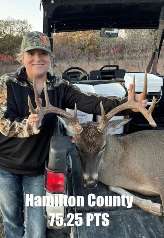 A woman is standing next to a deer in the back of a truck.