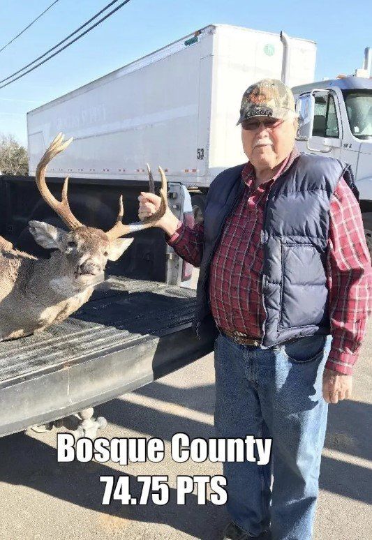 A man is standing next to a deer in the back of a truck.