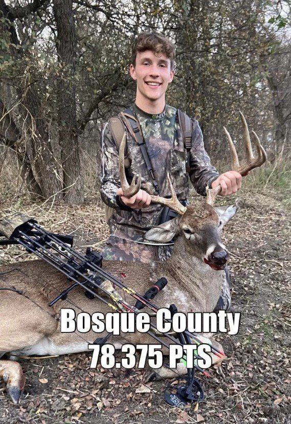 A young man in camo holds deer antlers, smiling, with a dead deer in Bosque County.