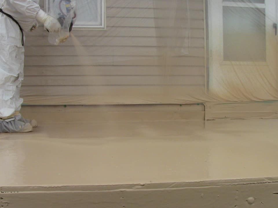 a man in a protective suit is spraying a concrete floor .