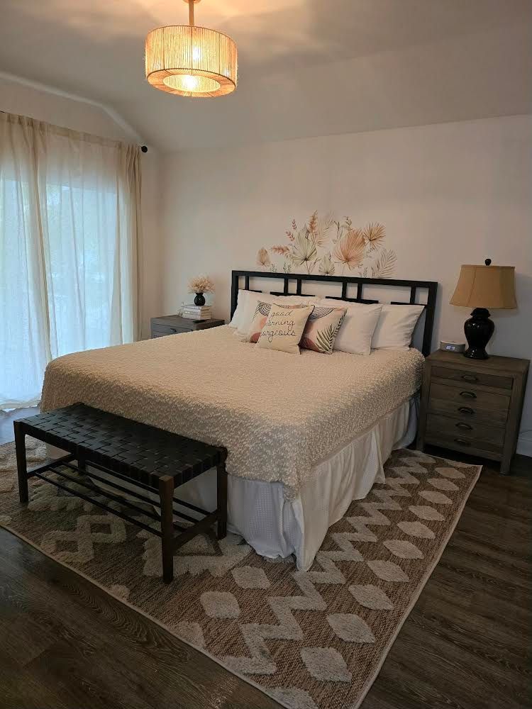 A bedroom with a bed , nightstand , rug and bench.