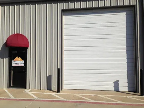 White garage door next to a black door with a red awning; building with metal siding.