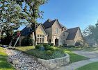 Large stone house with multiple gabled roofs, manicured lawn, and a stone-lined water feature.