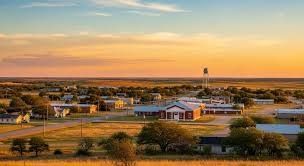 A white house with a black roof, porch, and cedar shake siding. Green lawn and blue sky.