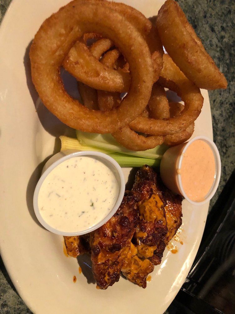 A white plate topped with chicken wings onion rings and dipping sauce