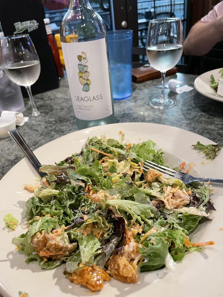 A white plate topped with a salad and a bottle of teaglass wine.