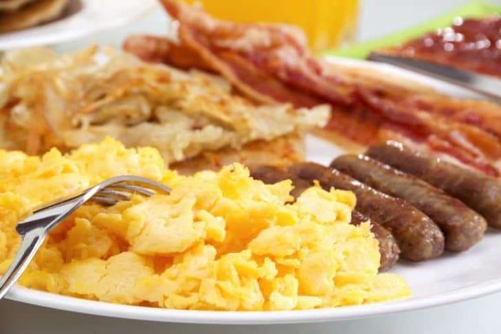 A white plate topped with scrambled eggs , sausage , bacon and hash browns.