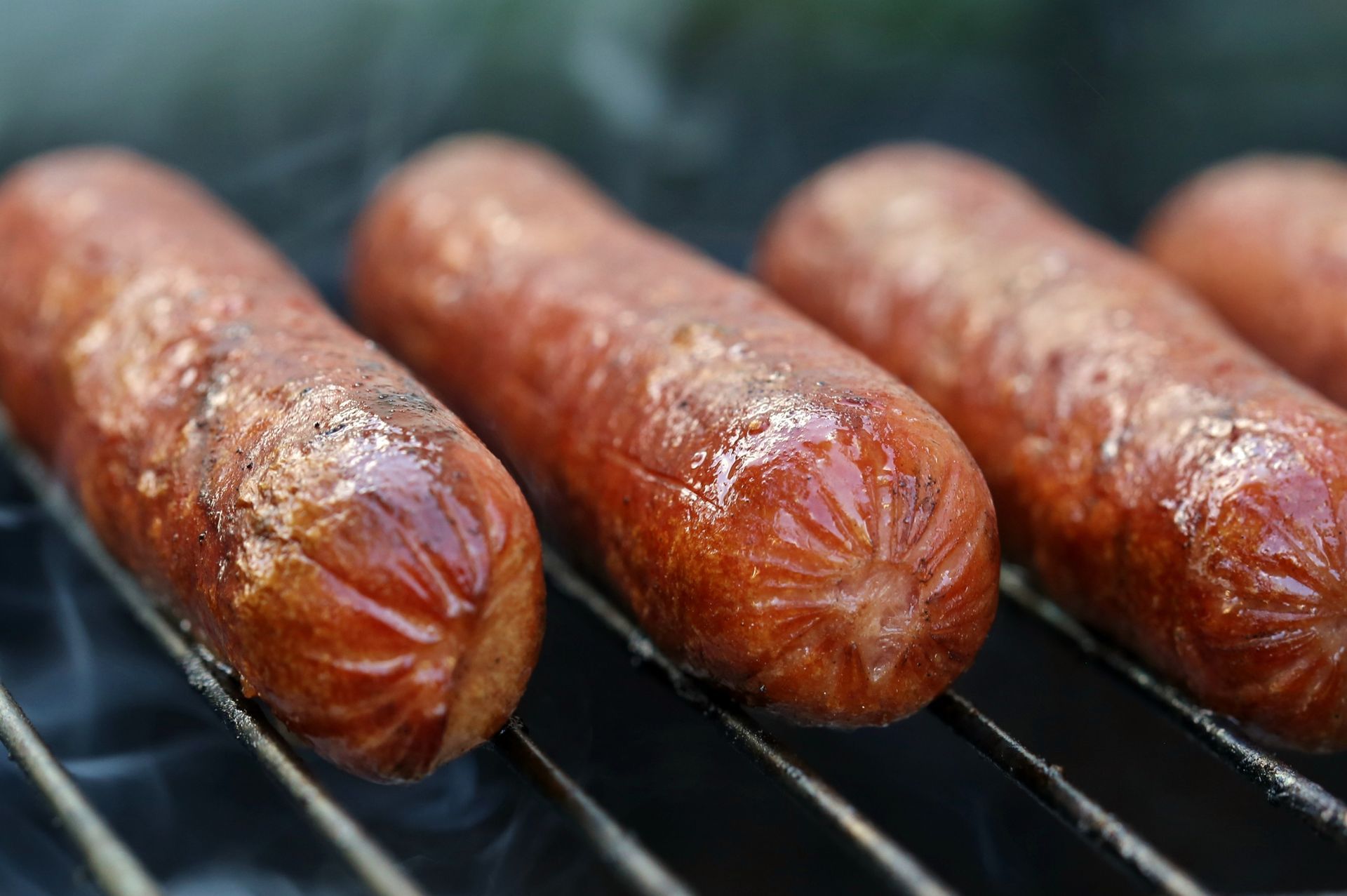 Four hot dogs are cooking on a grill.