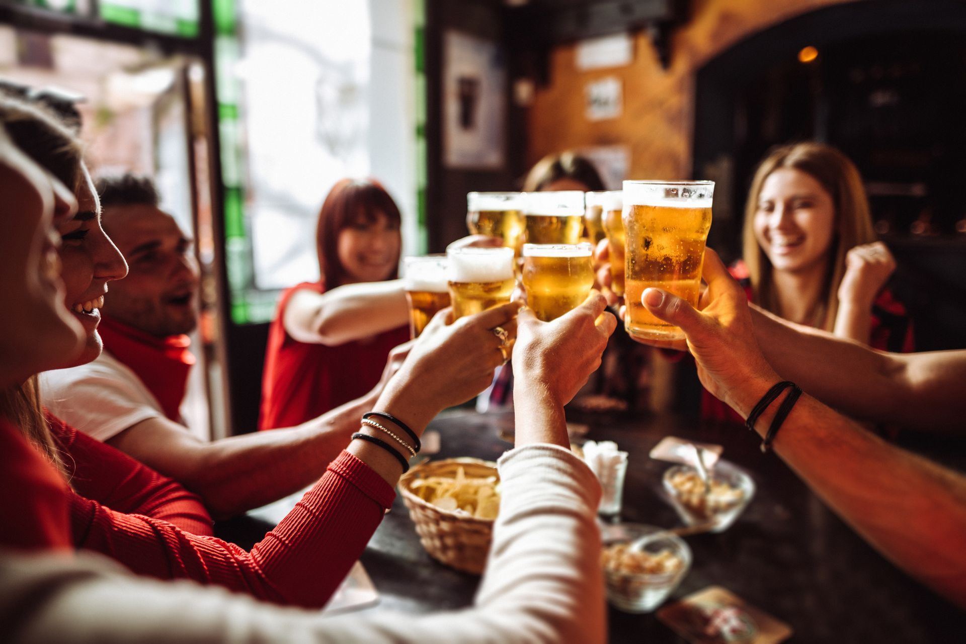 A group of people are toasting with beer in a bar.