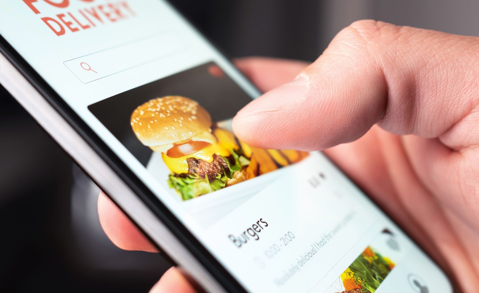 A person is holding a cell phone with a picture of a hamburger on the screen.