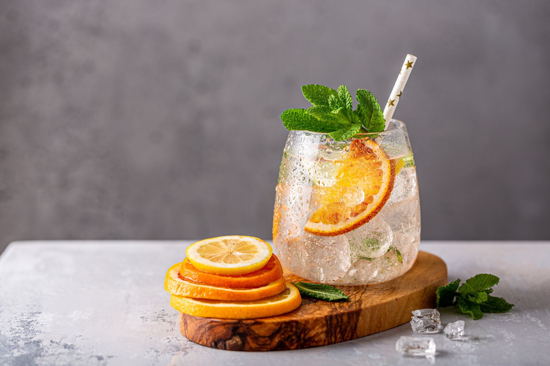 A glass of iced tea with orange slices and mint on a wooden cutting board.