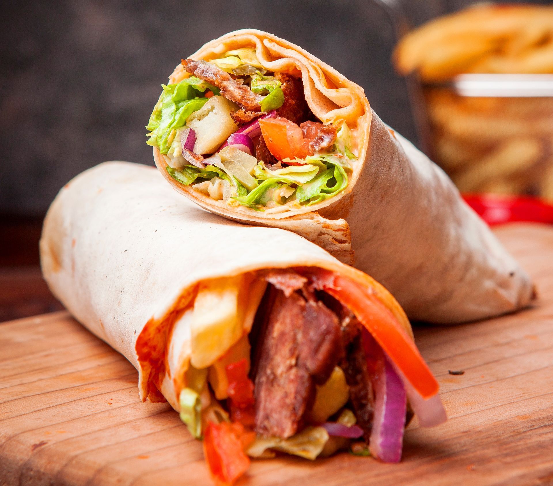 A wrap with meat and vegetables is sitting on a wooden cutting board.