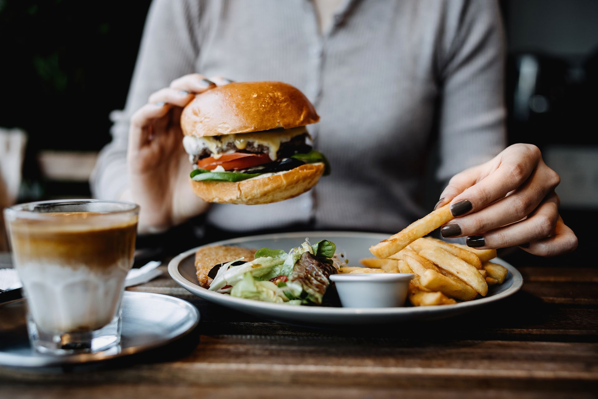 A woman is sitting at a table eating a hamburger and french fries.