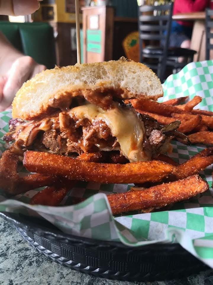A person is eating a hamburger with onion rings on top of it.