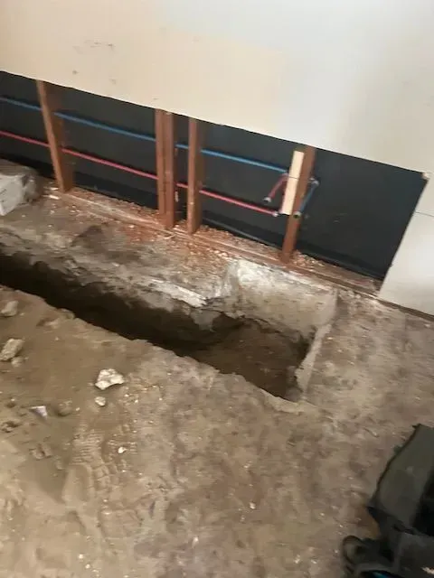 A hole in the floor next to a wall with pipes coming out of it.