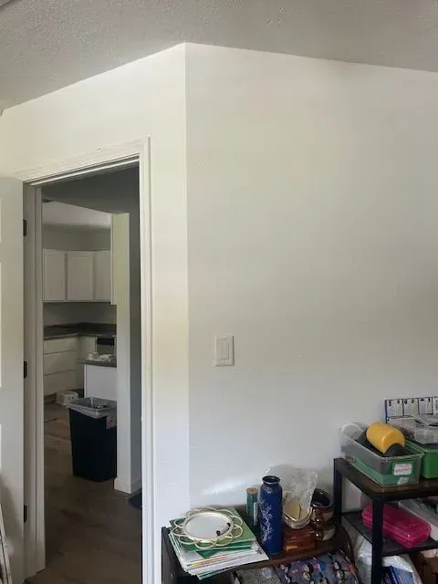 A room with white walls and a doorway leading to a kitchen.