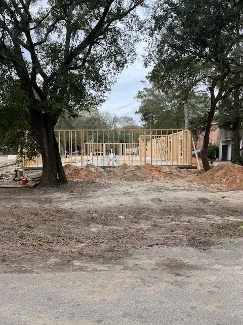 A house is being built in the middle of a dirt field surrounded by trees.