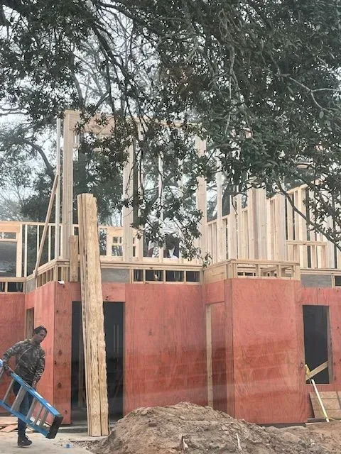 A man is carrying a ladder in front of a building under construction.