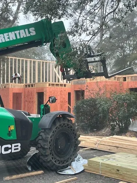 A green forklift is parked in front of a house under construction.