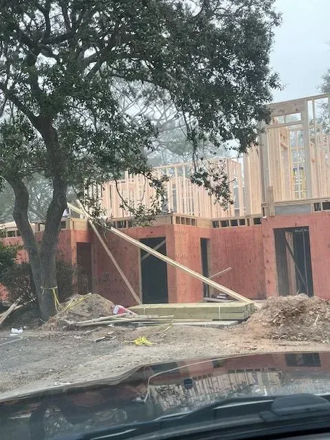 A house is being built on a dirt road next to a tree.