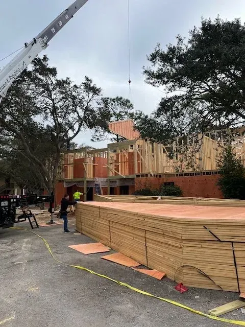 A crane is lifting a piece of wood in front of a building under construction