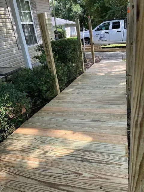A wooden walkway leading to a house with a truck parked in the background.