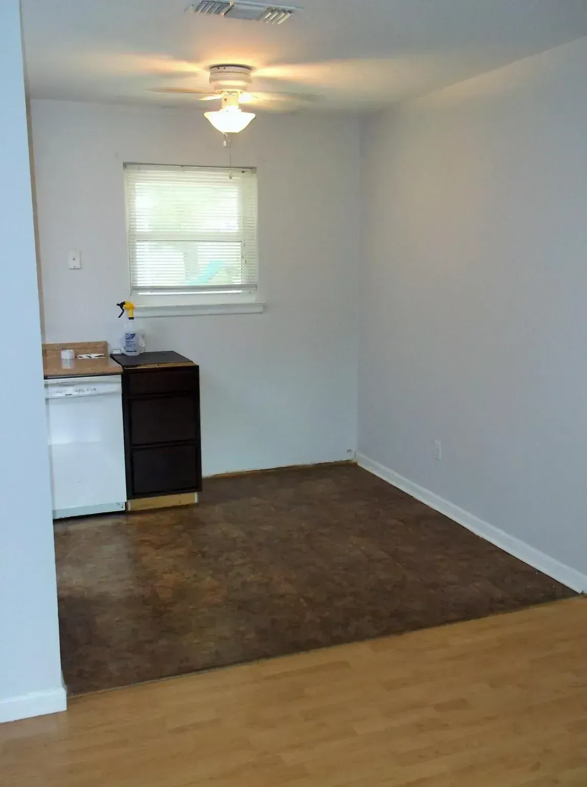 An empty room with hardwood floors , a dishwasher , and a window.