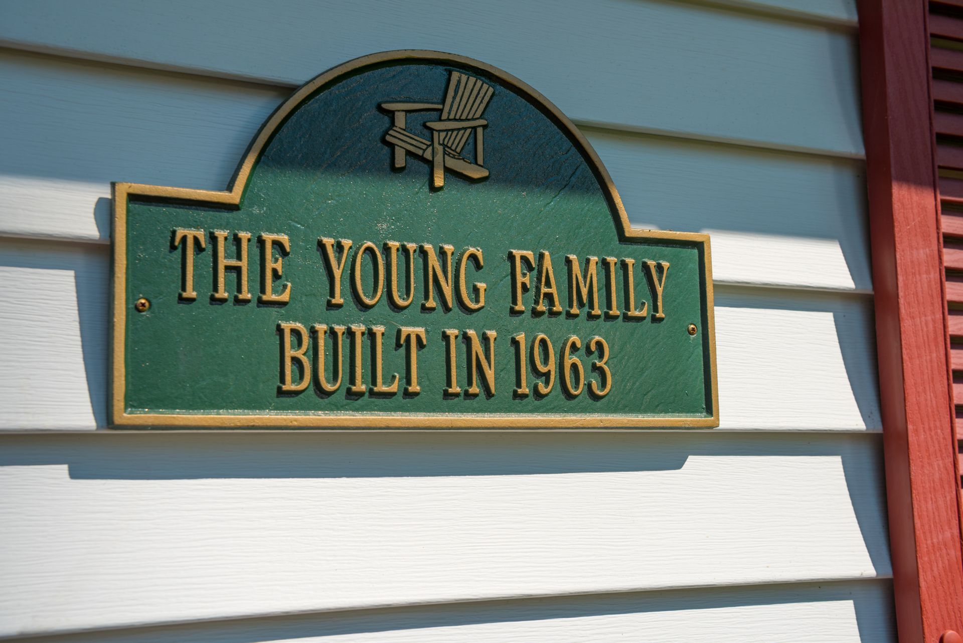 Green house plaque reading “THE YOUNG FAMILY BUILT IN 1963” on white siding