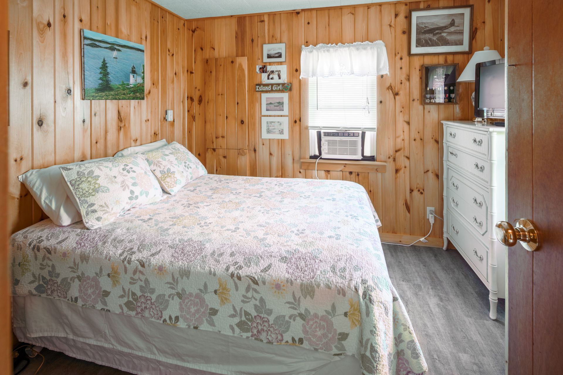 Cozy bedroom with wood-paneled walls, floral bedspread, window, and white dresser
