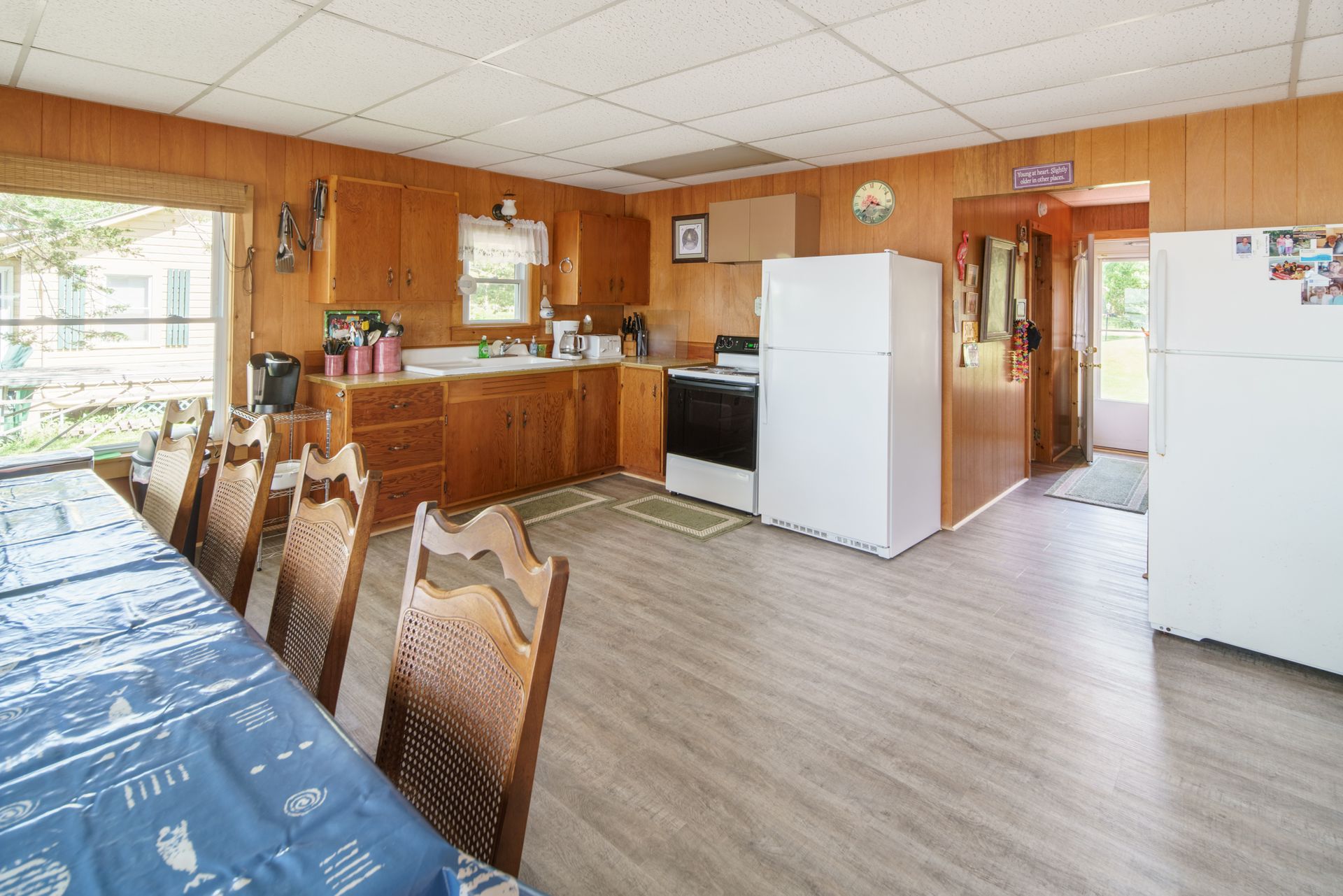 Wood-paneled kitchen with dining table, white appliances, and a doorway to another room