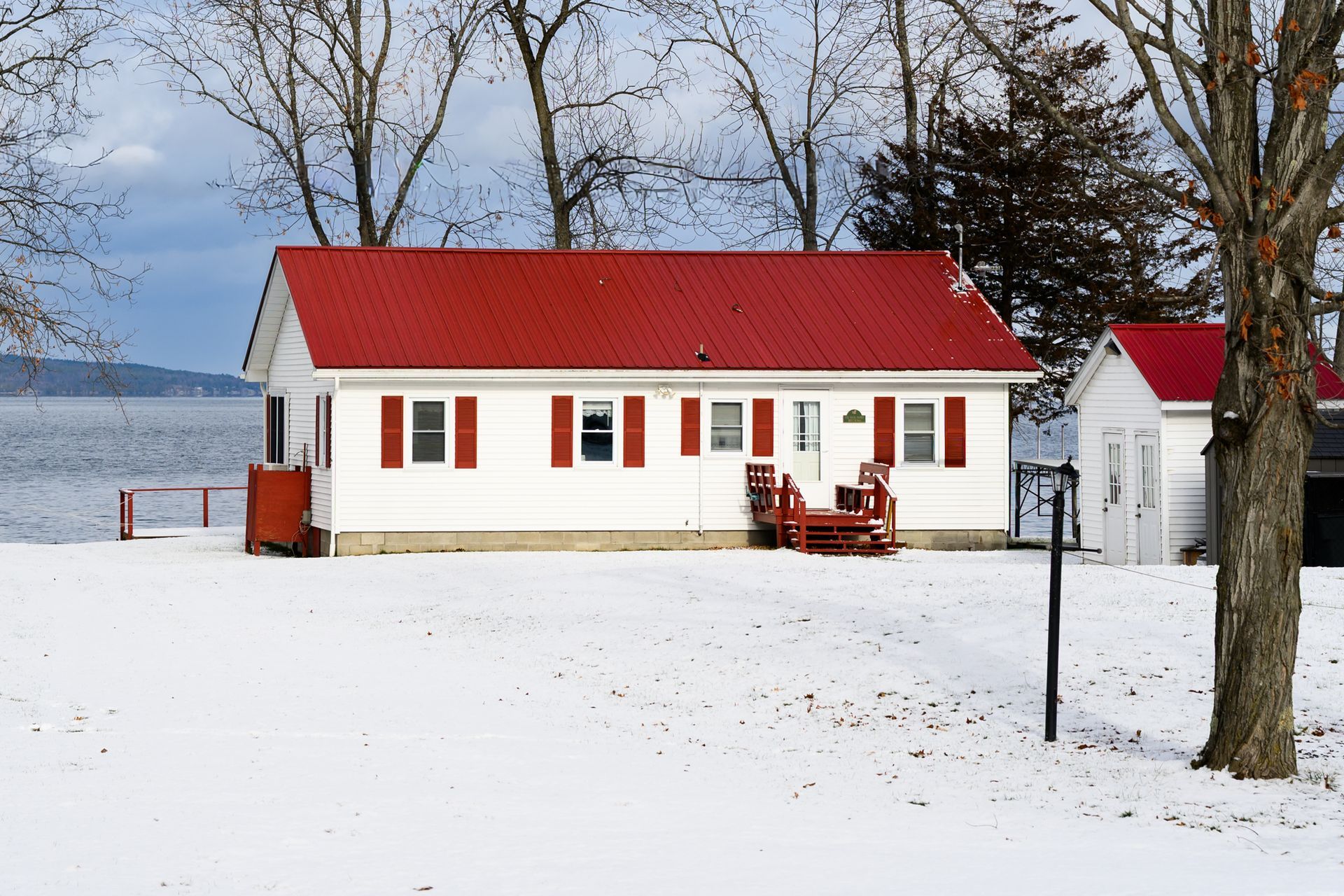 White lakeside cottage with red roof and shutters in a snowy winter landscape