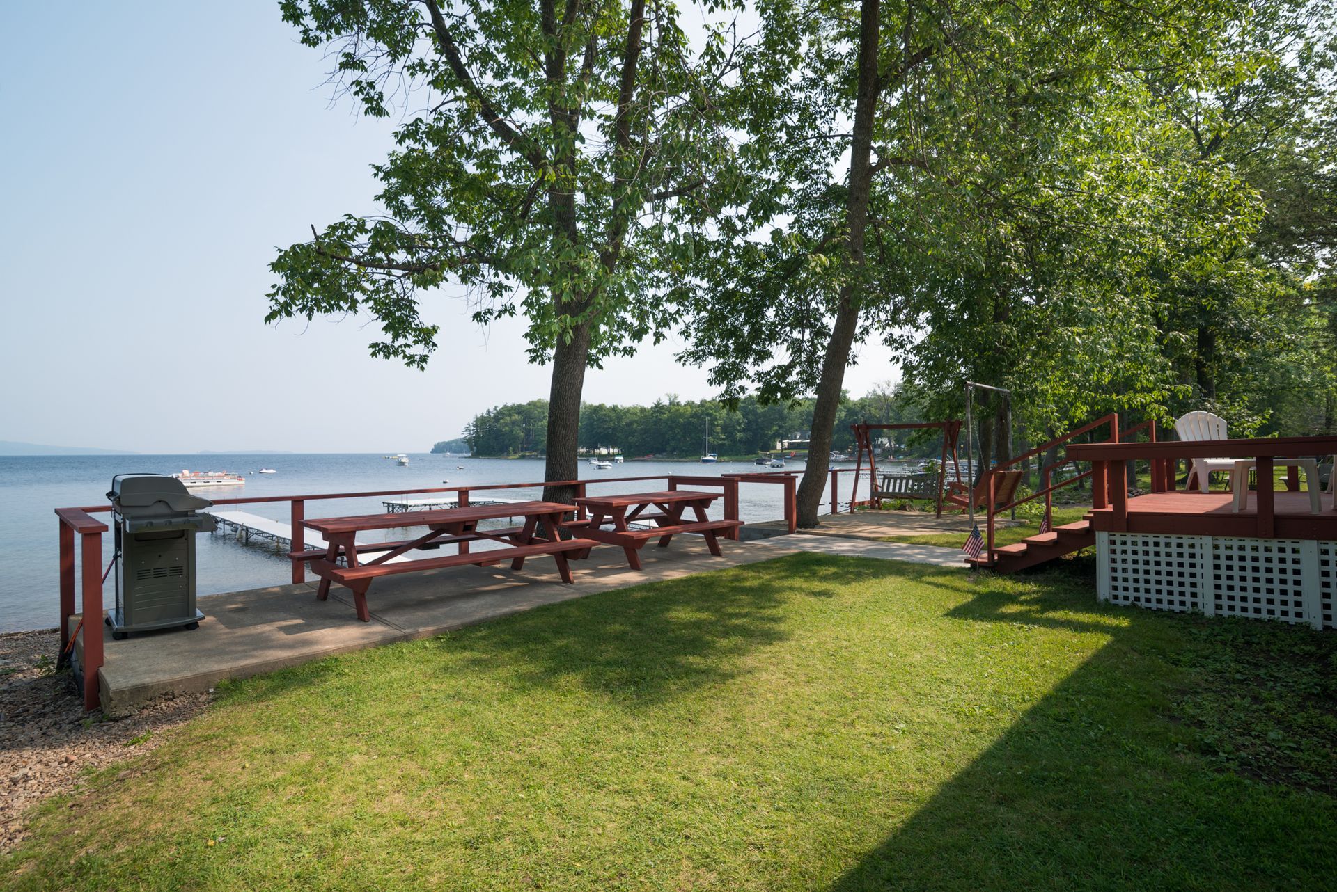 Lakeside park with picnic tables, trees, and a grassy shore under clear skies