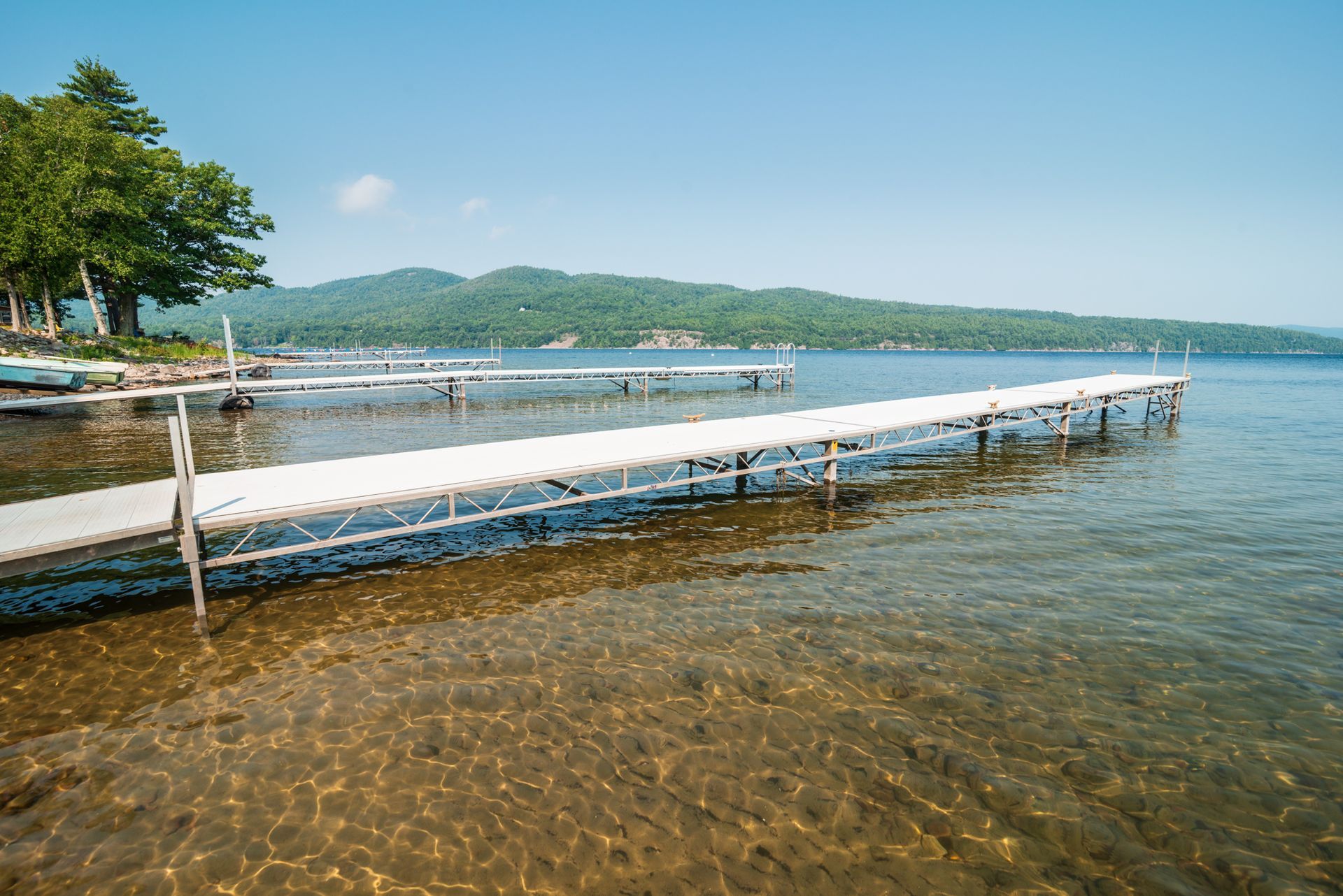 Long white floating dock extending over clear blue lake with forested hills in the background