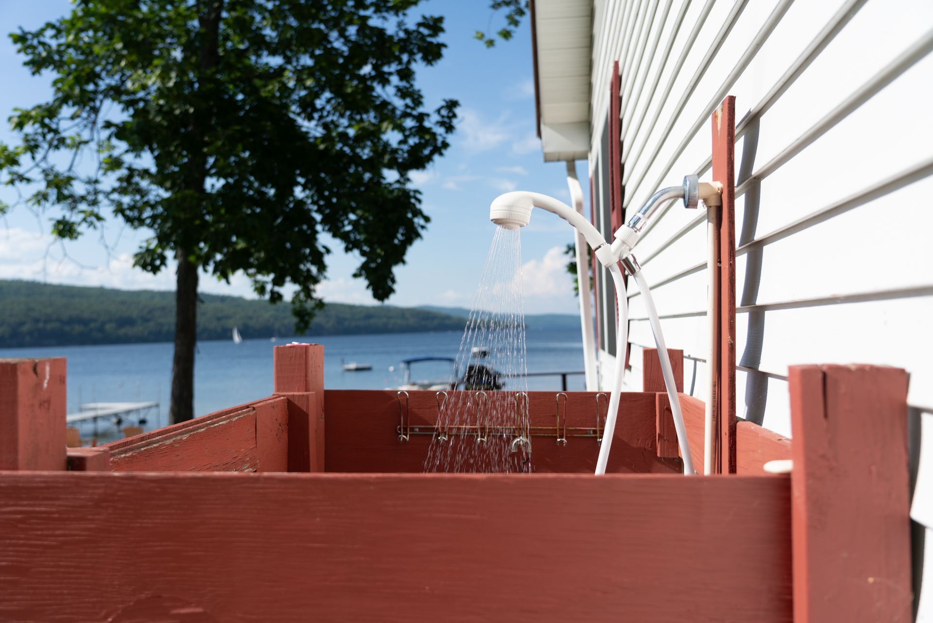 Red wooden deck with white siding, a sprinkler spraying water, and a lake view in the background
