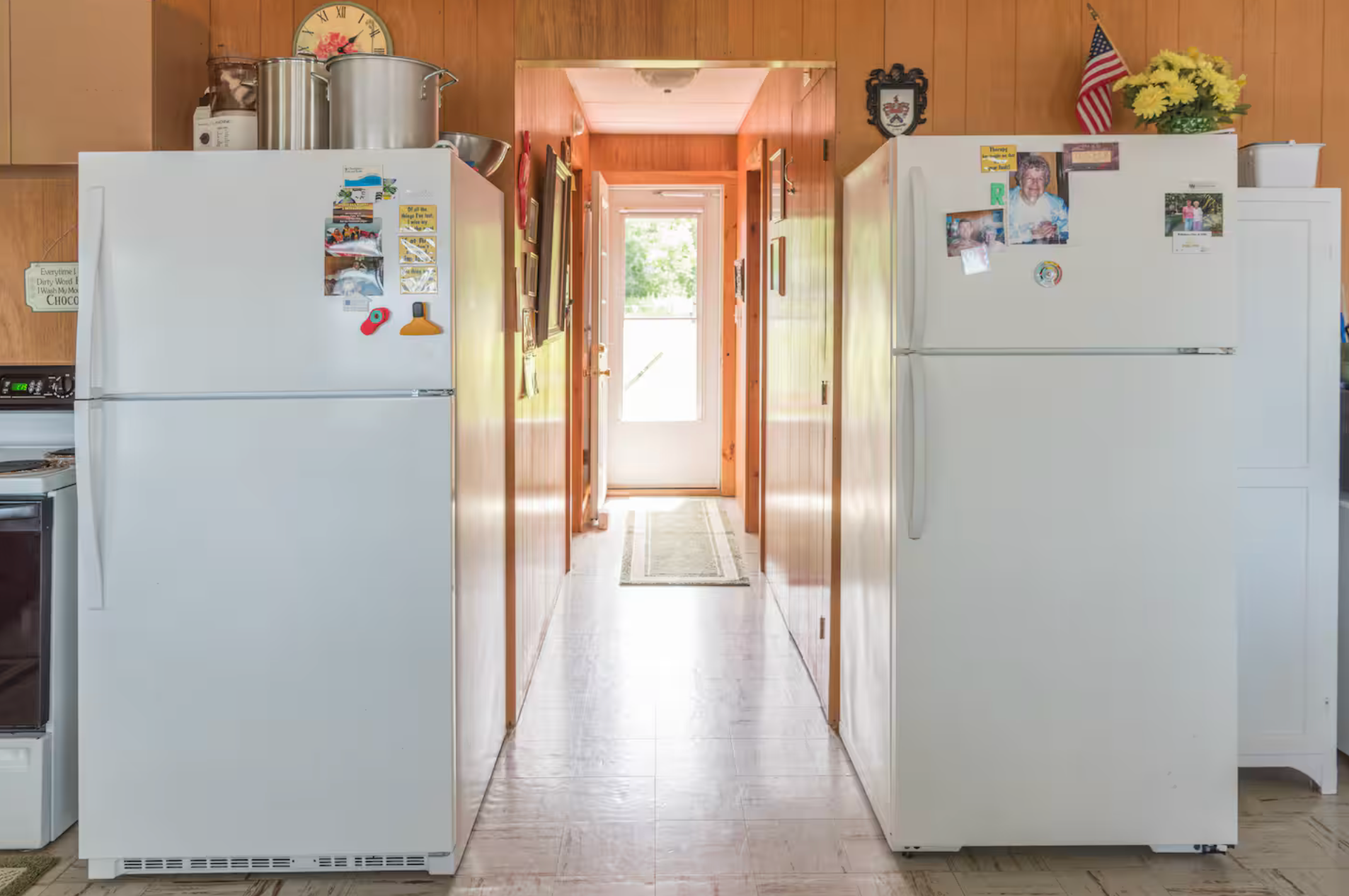 Two white refrigerators in a bright kitchen hallway, one on each side of a narrow walkway.