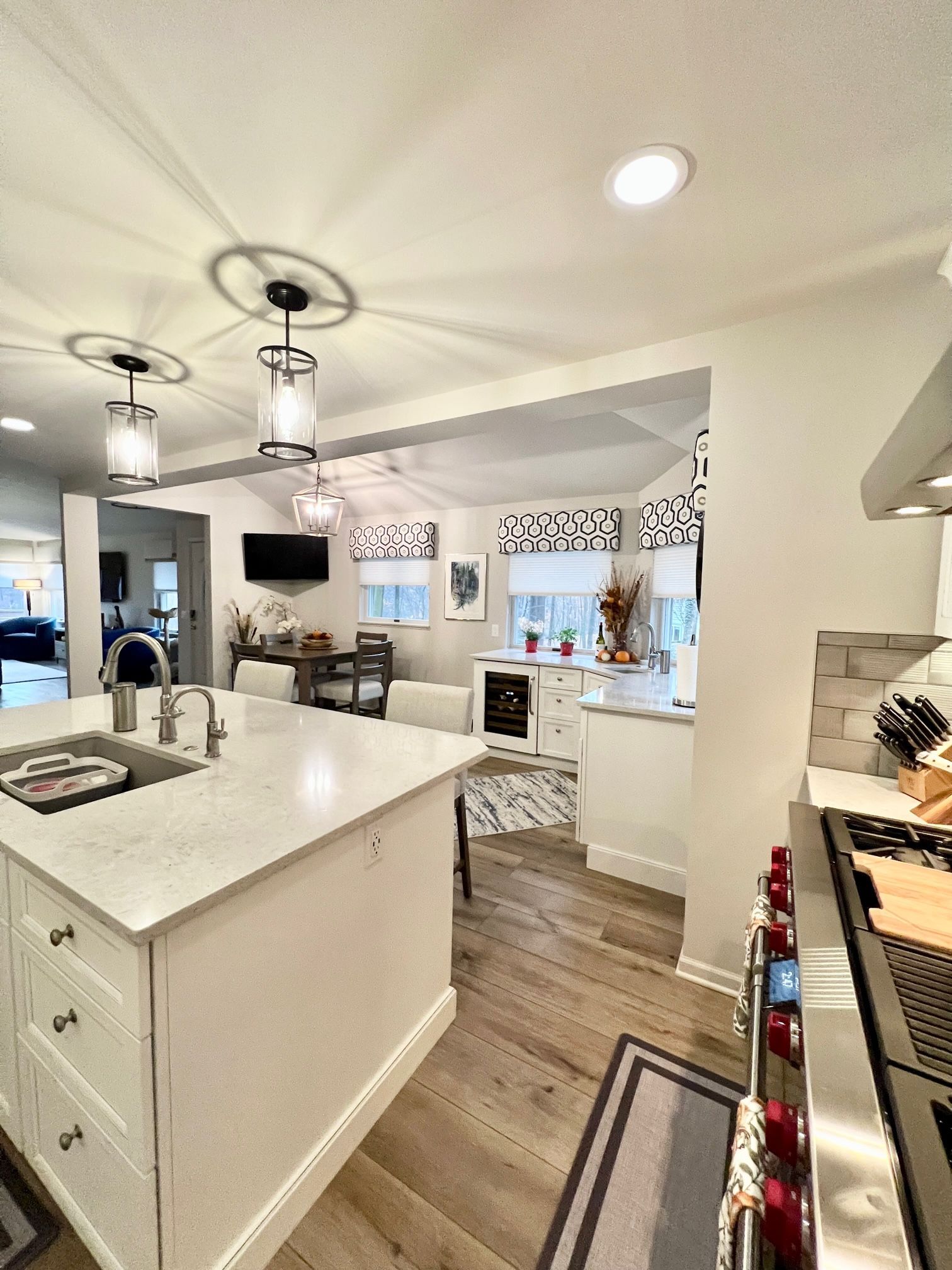 A kitchen with a large island, sink, stove and stainless steel appliances and window treatments.