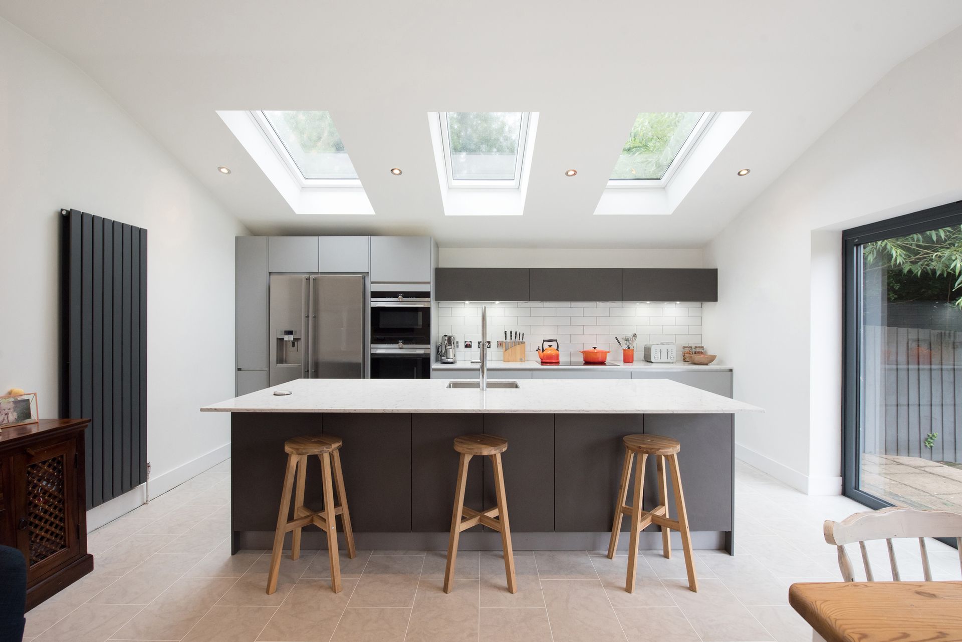 A kitchen with a large island , stools , a table and skylights