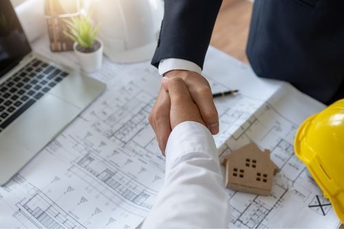 Two men are shaking hands over a blueprint of a house