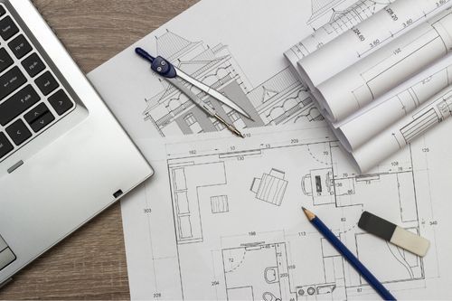 A laptop computer is sitting on top of a wooden table next to a bunch of drawings