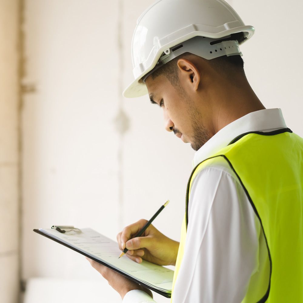 A man wearing a hard hat and safety vest is writing on a clipboard