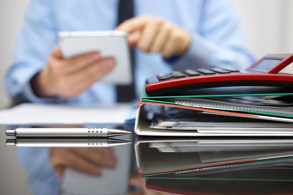A Man Is Sitting At A Desk Using A Cell Phone And A Calculator — NQ Business Advisers In Jensen, QLD