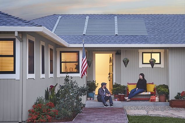 A man and a woman are sitting on the porch of a house with solar panels on the roof.