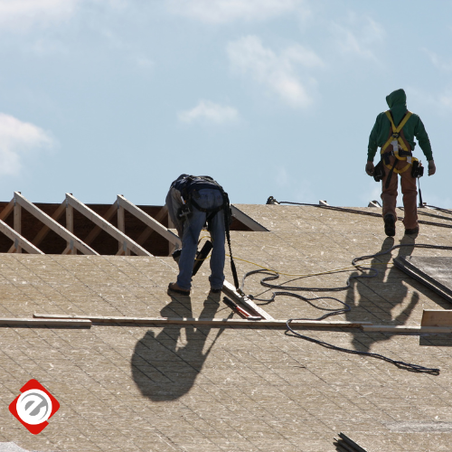 Two construction workers on a rooftop installing sheathing on a sunny day.