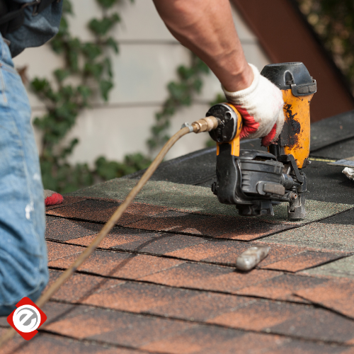 Roofer using a nail gun to secure shingles on a brown roof.