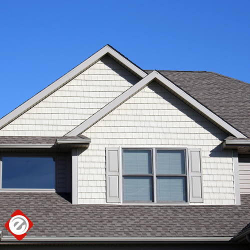Gabled roof of a house with white shingle siding and gray trim against a clear blue sky.