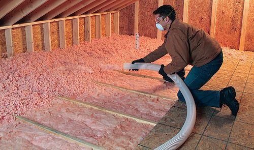 A man is blowing insulation into an attic with a vacuum.